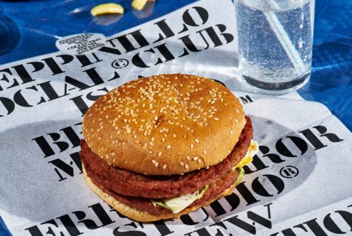 Realistic burger mockup on newspaper ad design with glass of water, ideal for showcasing food-related graphics and branding projects.