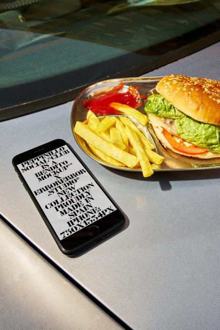 Smartphone mockup with typographic design on screen beside a plate with burger and fries, ideal for food app design presentations.