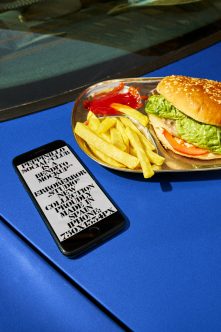 iPhone mockup on bright blue surface next to burger meal with fries