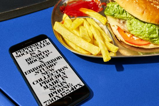 Smartphone with typography mockup on screen beside a juicy burger and fries on blue background for graphic design showcase.