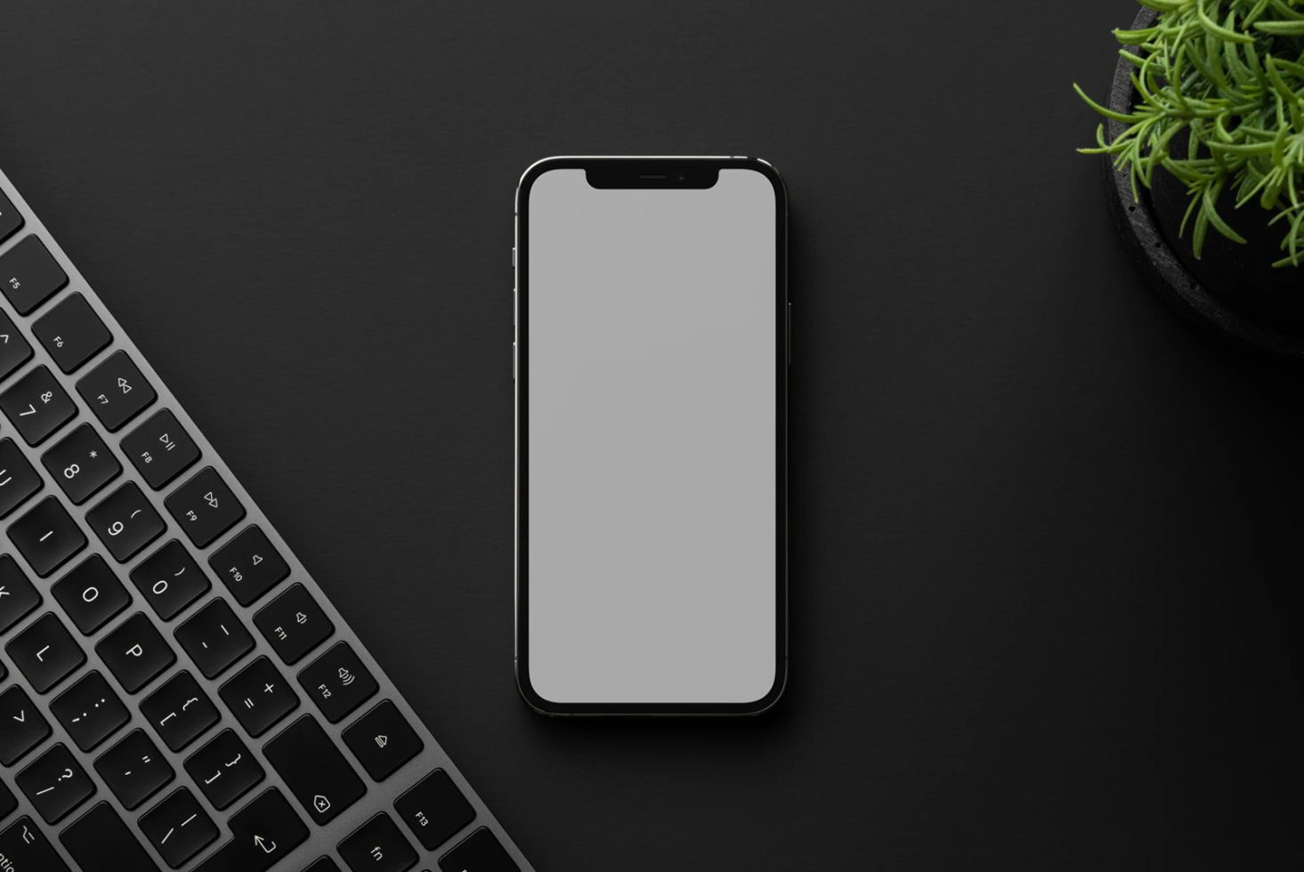 Mockup of smartphone on a dark surface next to keyboard and plant, ideal for showcasing app designs and user interfaces.