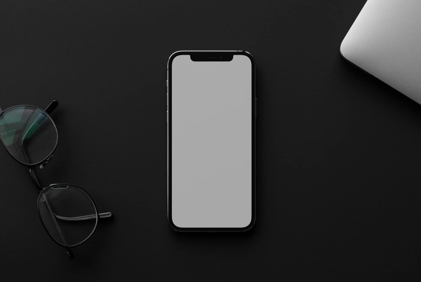 Modern smartphone mockup on dark background with sunglasses and laptop corner, ideal for design presentation and digital asset.