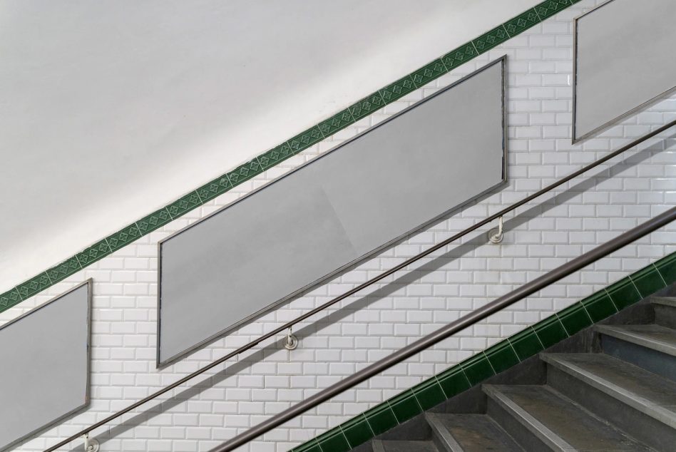 Modern stairwell with white subway tiles, green trim stripes, metal railings with blank signage spaces