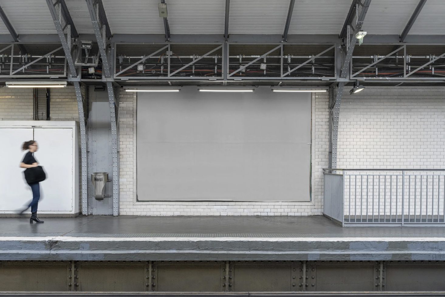 Blank billboard at a subway station platform with a blurred person walking by, ideal for advertising mockup designs for urban settings.