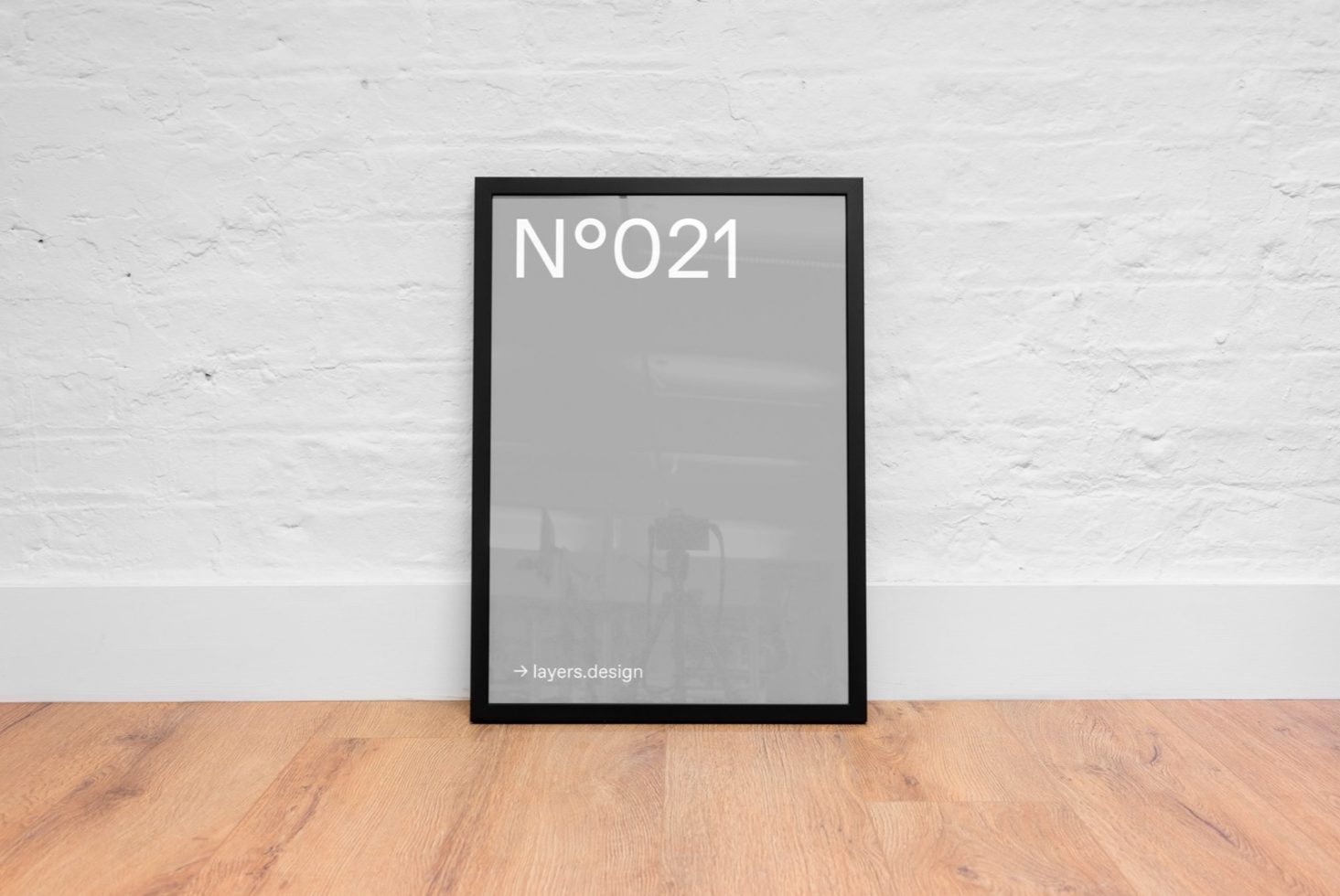 Modern black picture frame mockup against a white brick wall on wooden floor, ideal for posters and art display in interior design.