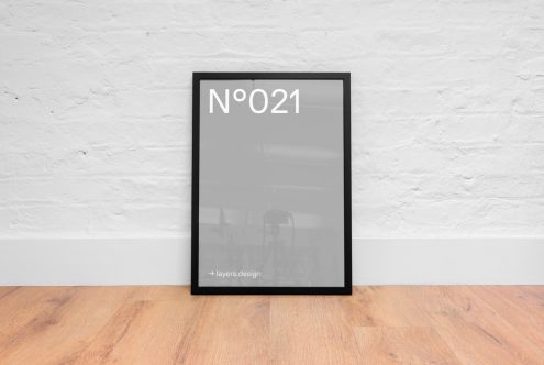 Modern black picture frame mockup against a white brick wall on wooden floor, ideal for posters and art display in interior design.