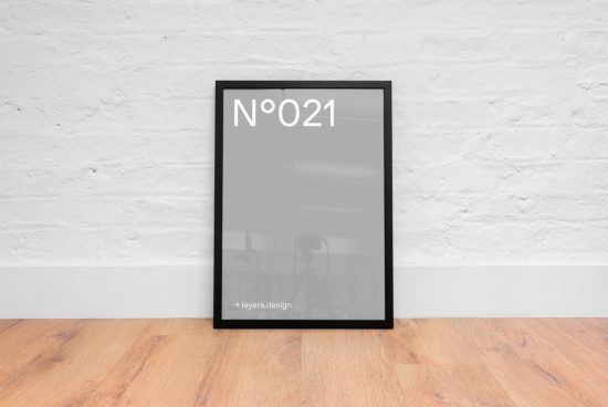 Modern black picture frame mockup against a white brick wall on wooden floor, ideal for posters and art display in interior design.