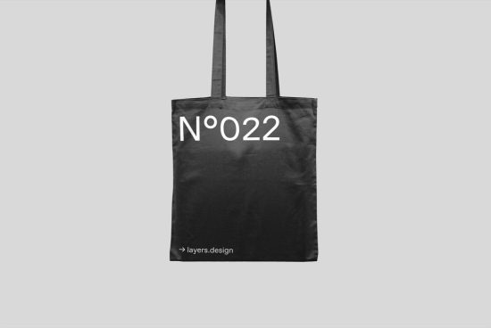 Black tote bag mockup with minimalist white text design, hanging against a grey background, displaying a unique number, by layers.design for branding.