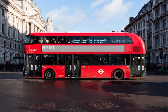 Red London double-decker bus in urban setting for transport mockup or template design, clear daylight with city architecture background.