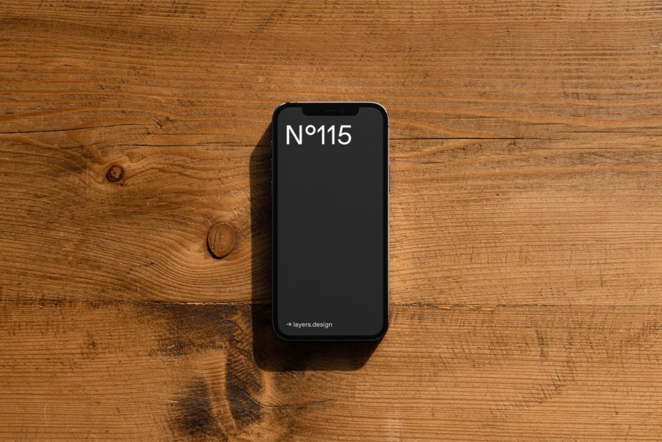Black iPhone with N°115 on screen resting on rustic wooden table