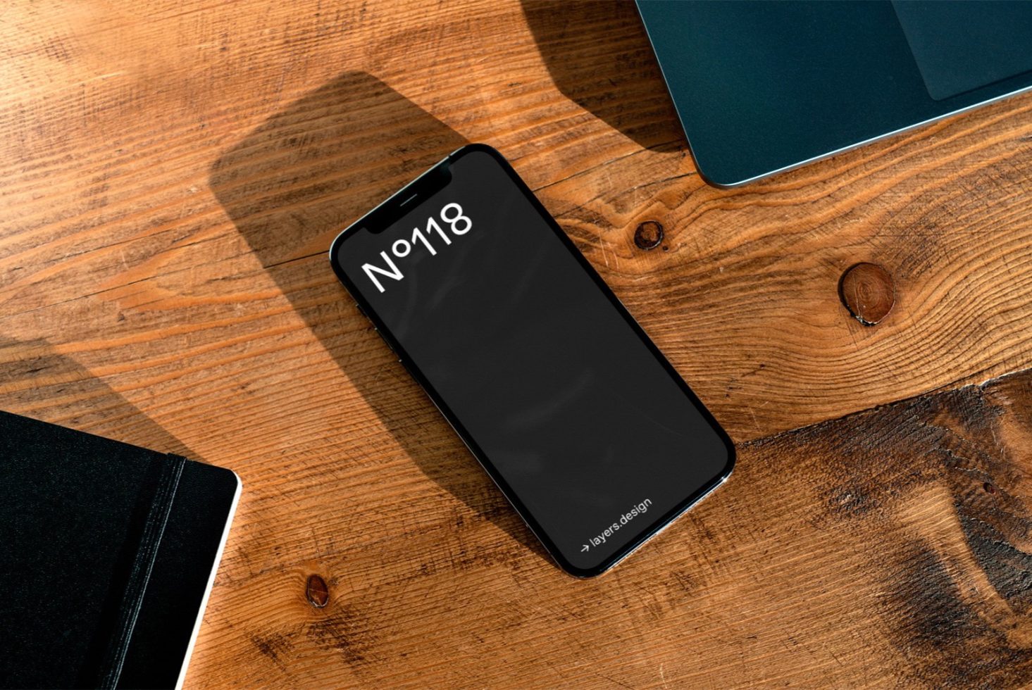 Smartphone mockup on wooden desk next to notebook and tablet, ideal for UI design presentation and digital asset portfolio.