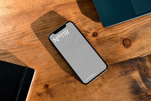 Smartphone mockup on wooden desk next to laptop and notebook, perfect for designers to showcase mobile app designs.