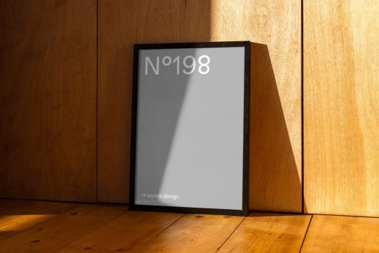 Modern poster mockup in a frame leaning against a wooden wall with sunlight casting a dynamic shadow, perfect for showcasing design work.