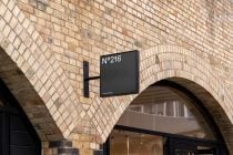 Square sign hanging on brick wall above arched storefront entrance