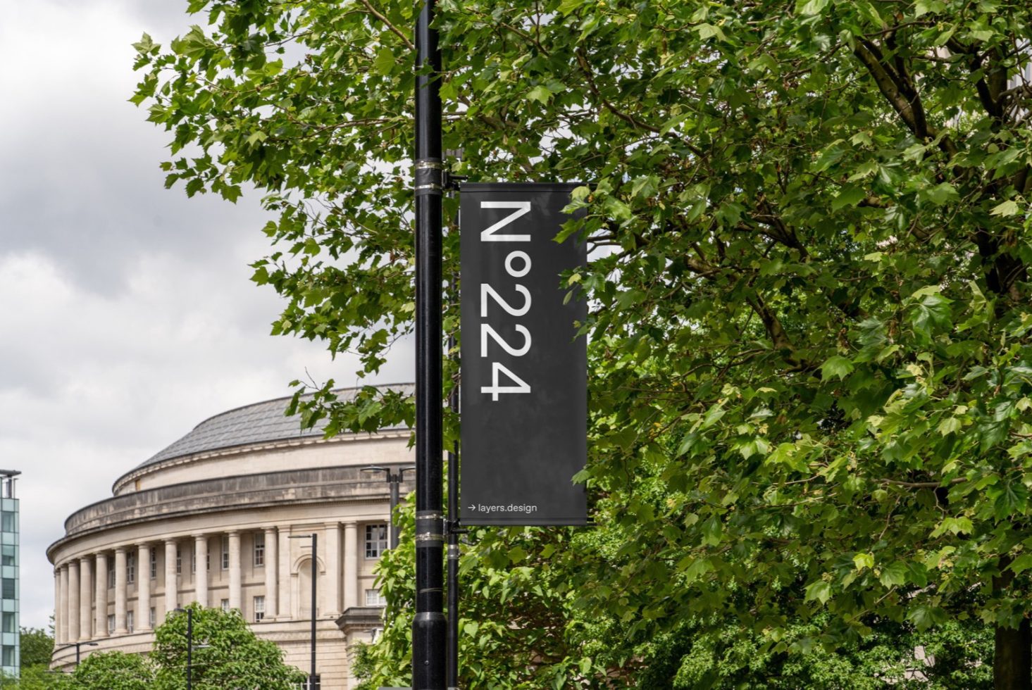 Outdoor banner mockup with a neoclassical building in the background, surrounded by lush green foliage, suitable for branding designs.