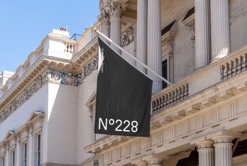 Black flag mockup hanging on classic building with columns, clear sky background, design digital asset, editable banner graphic display template.