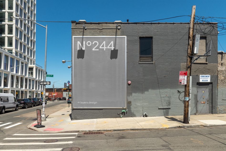 Downtown street corner with gray billboard showcasing N°244 on industrial building