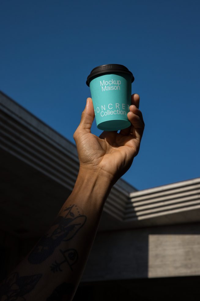 Hand holding a custom coffee cup mockup with a clear sky background, ideal for branding presentations and design assets.