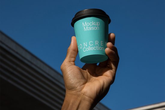 Hand holding a teal coffee cup mockup with custom branding against a clear blue sky, ideal for designers to showcase logos and designs.