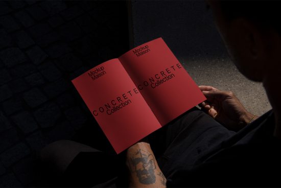 Person holding open brochure mockup with red cover design, showcasing custom font on a concrete textured background, ideal for graphic presentations.