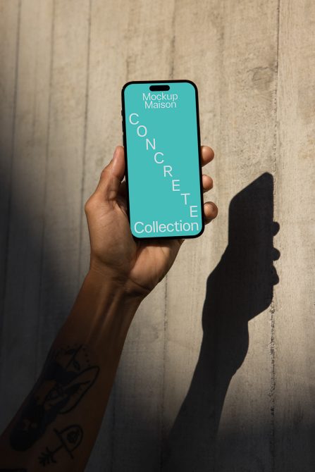 Smartphone screen mockup held in hand against textured concrete wall, with shadow, displaying design label, suitable for showcasing app interfaces.