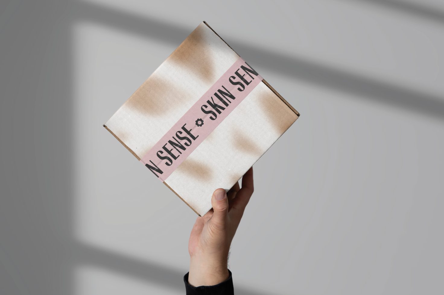 Hand holding a cardboard box with modern branding mockup against a shadowy background for product packaging design presentation.