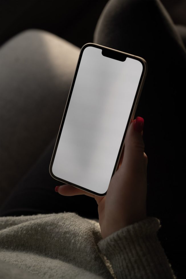 Hand holding smartphone with blank screen mockup for app design presentation, in a muted light setting, digital asset for designers.