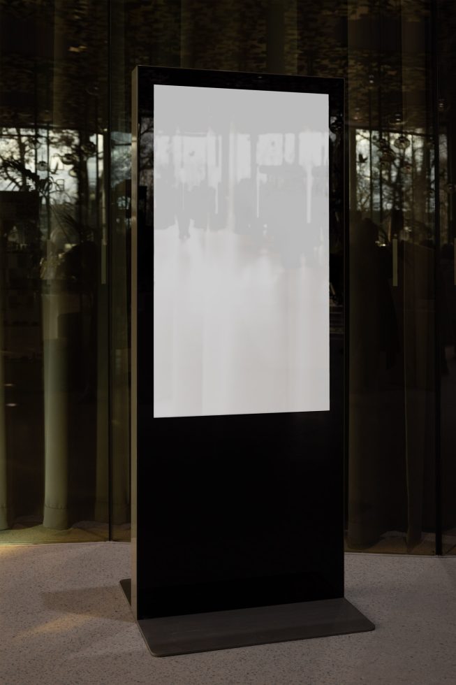 Vertical digital signage display mockup in a modern office lobby with reflective glass background for advertising design presentations.