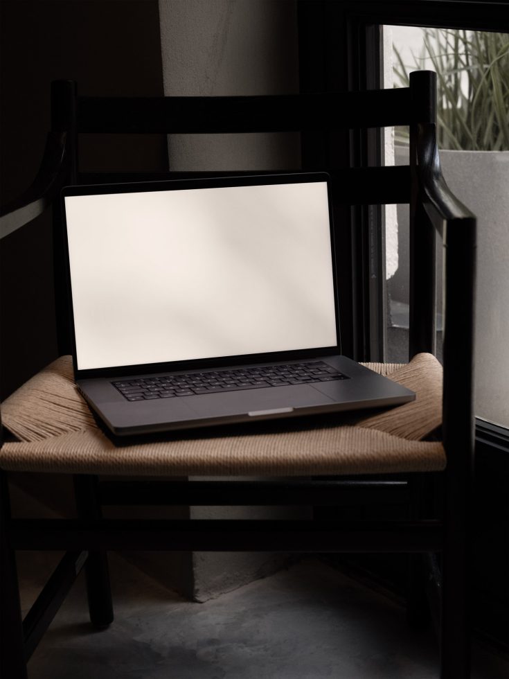 Laptop with blank screen on a wooden chair, modern minimalistic design, ideal for mockups and templates in a creative workspace.