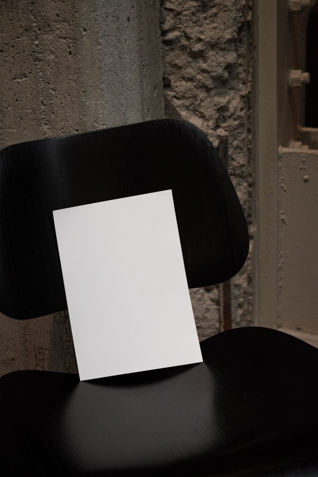 Blank white vertical card mockup on a black chair with textured background, ideal for presentation designs and brand identity visuals.