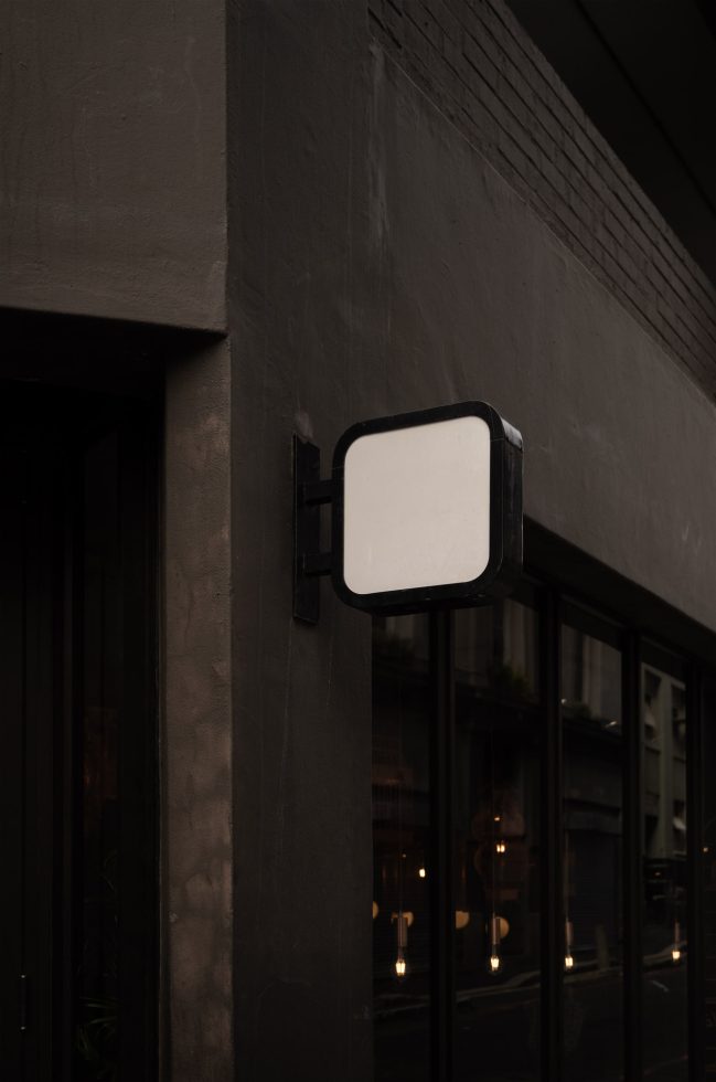 Blank square urban signboard mockup on a building corner, ideal for logo presentation and branding design, with dark moody lighting.