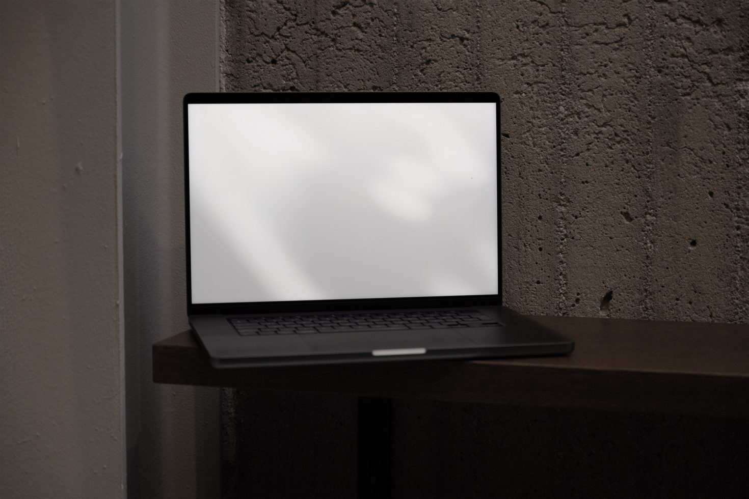 Laptop with blank screen on a wooden shelf against a textured grey wall, ideal for mockups, website design, and digital assets.