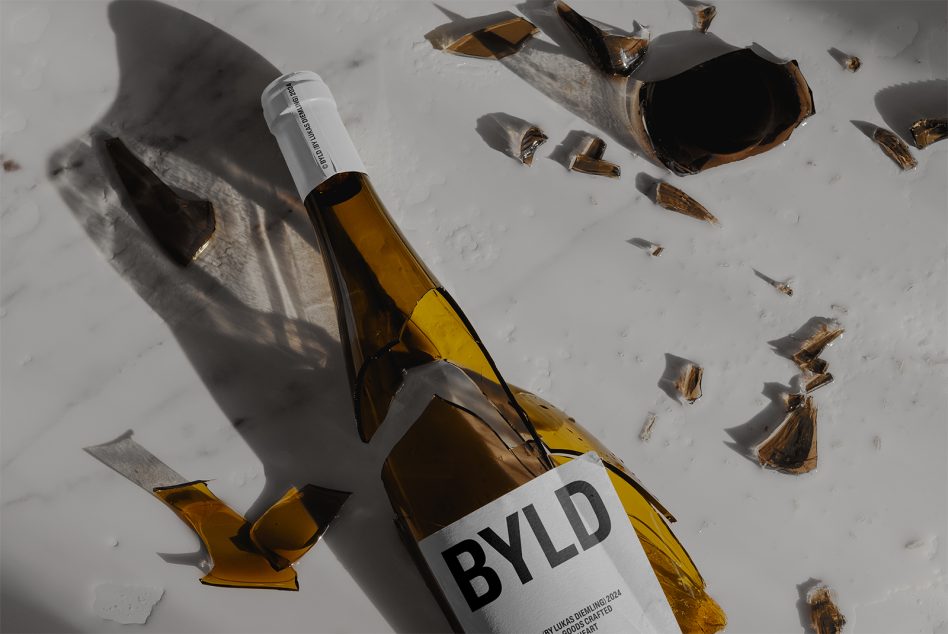Two broken beer bottles with white labels showing BYLD branding surrounded by shards