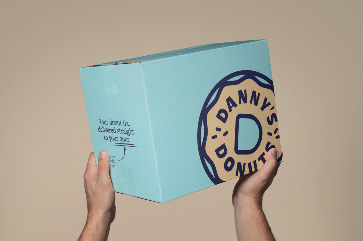 Hands holding a custom blue packaging box with branding mockup for Danny's Donuts, ideal for designers creating product packaging templates.