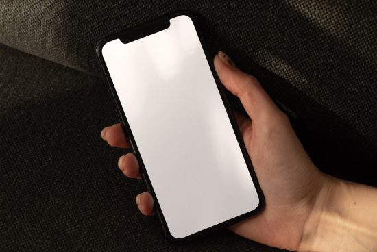 Hand holding smartphone with blank screen on dark texture for mockup design presentation, device screen mockup, digital asset.