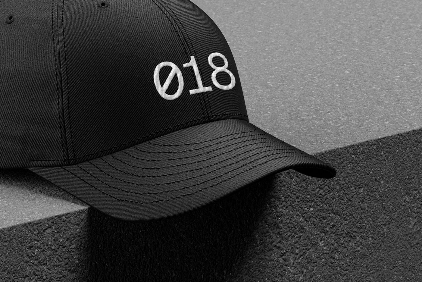 Black baseball cap mockup with white embroidered numbering 018 on textured background, detailed close-up for fashion and apparel designs.