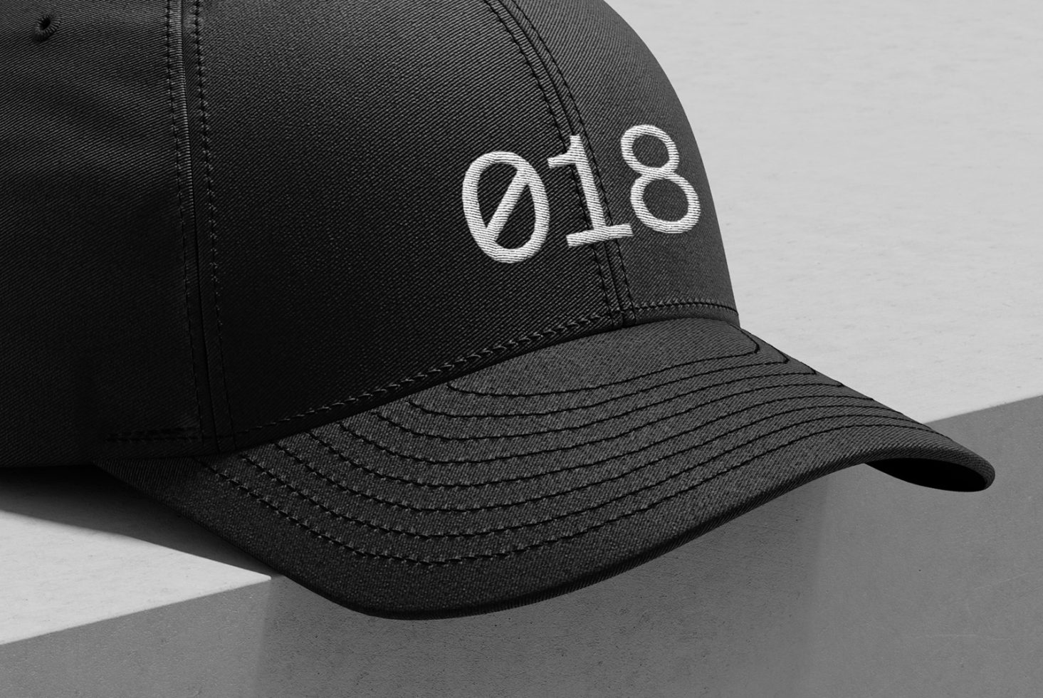 Black baseball cap mockup with white embroidery design 018, showcasing texture and shadows for realistic graphic presentation.