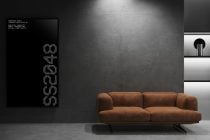 Vertical screen mockup with pixelated text beside tan sofa in minimalist concrete gallery