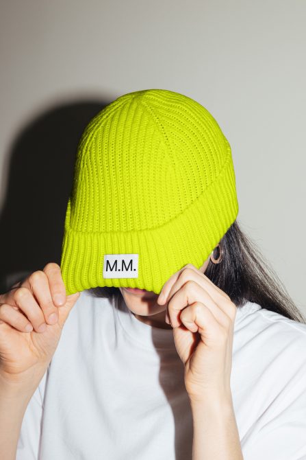 Person wearing vibrant yellow beanie covering eyes, focus on fabric texture and label detail, ideal for fashion mockups.