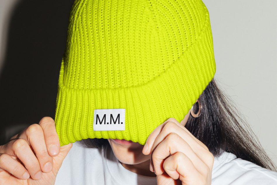 Person pulling down neon green beanie mockup with logo, trendy headwear design, versatile fashion accessory graphic.