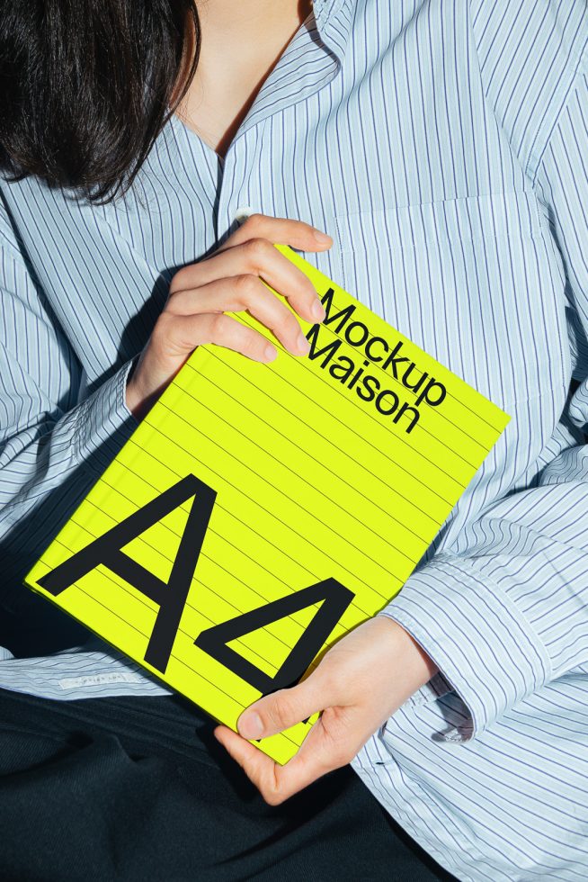 Person holding a bright yellow A4 mockup with black letters, ideal for graphic design presentations, in a striped shirt, design resource.