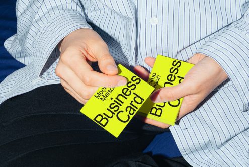 Person holding neon yellow business card mockup, striped shirt and black pants, design showcase, editable template graphic.