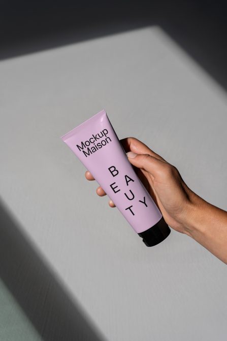 Hand holding a tube of beauty cream, labeled Mockup Maison. Ideal for product mockup presentations, beauty product branding, and packaging design.