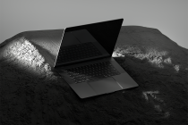 Dark laptop mockup on rocky terrain with studio lighting