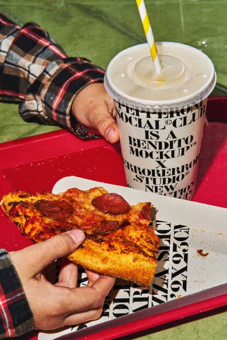 Pizza mockup design featuring a person's hand holding a slice of pepperoni pizza with a soda cup in the background. Ideal for food-related graphics.