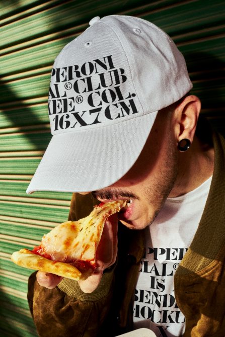 Man in graphic t-shirt and cap eating pizza. Designer t-shirt mockup clothing template fashion mockup apparel merchandise. Perfect for showcasing designs.