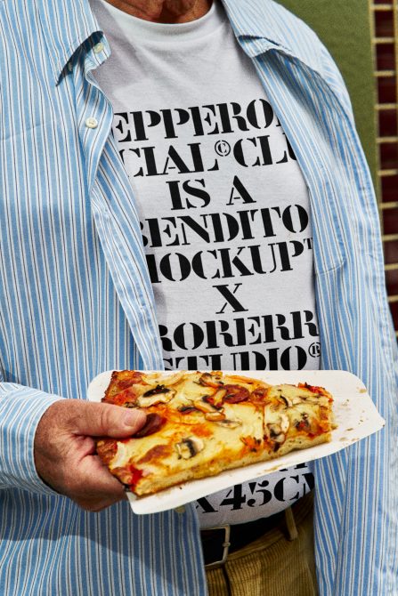 Man in striped shirt holding pizza slice, wearing a white t-shirt with bold black text design. Ideal for t-shirt mockups and graphic design templates.