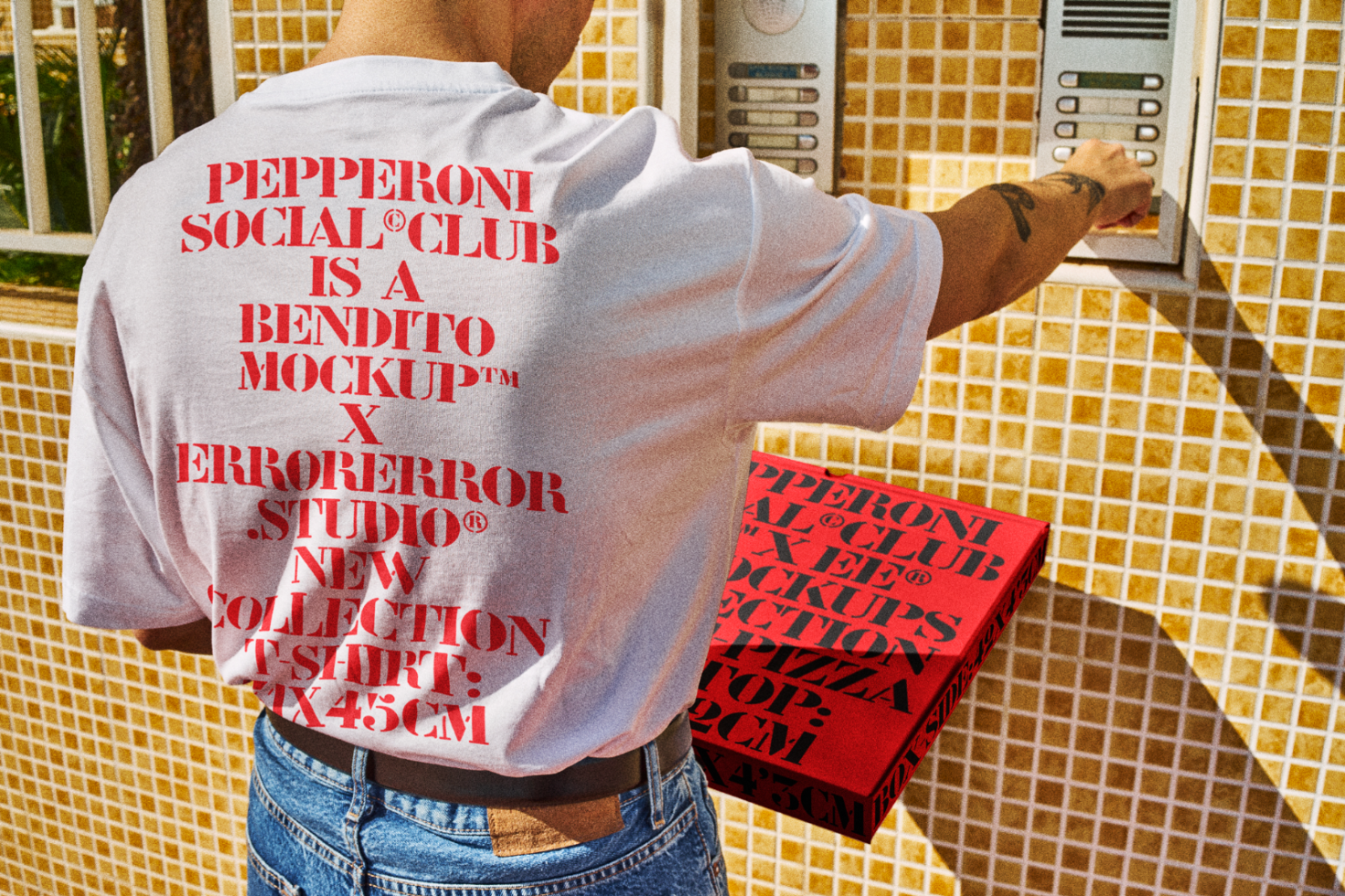 Man wearing white T-shirt with red graphics text, holding a red pizza box, standing near intercom system; stylish apparel mockup for graphic designers.