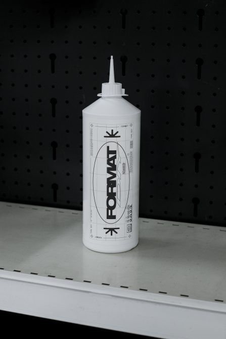 White squeeze bottle labeled FORMAT with geometric design, placed on shelf against pegboard background. Suitable for Designers seeking Mockups, Templates for product design.