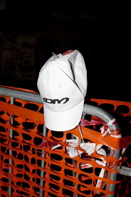 White baseball cap with a logo hanging on an orange construction barrier at night. Perfect for graphics and mockups. Urban streetwear design inspiration.